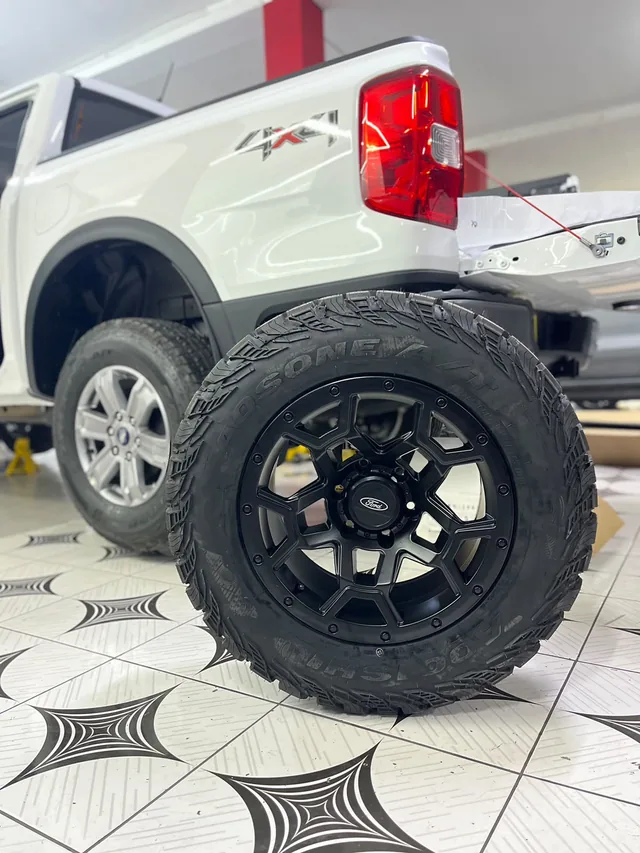 Aro negro con neumático junto a una camioneta blanca en BARMARE