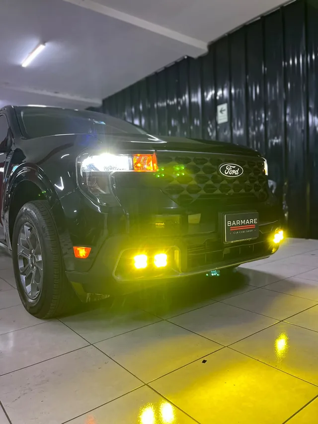 Ford negra con luces auxiliares amarillas encendidas y placa de exhibición BARMARE