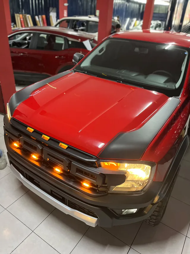 Camioneta Ford roja con detalles oscuros en el capó y luces ámbar en la parrilla